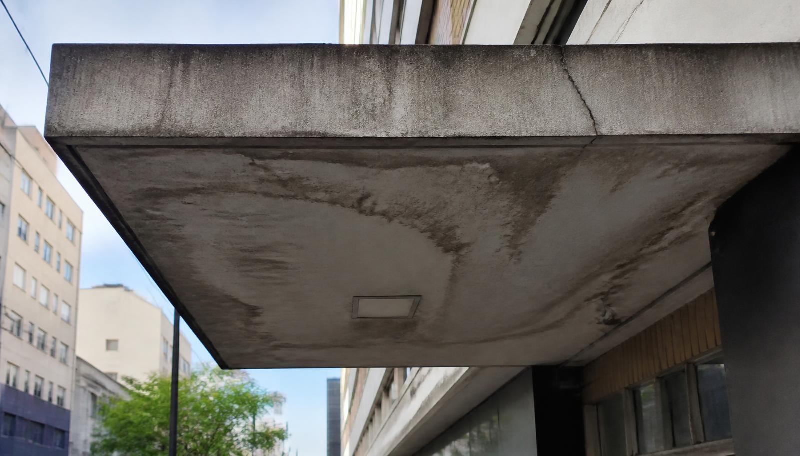 Inspeção técnica de marquise de concreto na entrada de edifício, com verificação de fissuras e drenagem